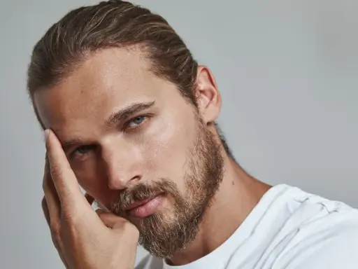 Un homme pensif, sa main effleurant son front, un sourcil plus haut que l'autre, regard intense.