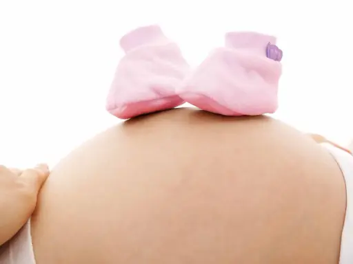 Close-up of a pregnant belly with tiny pink baby booties on top.