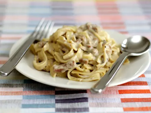 Un piatto di tagliatelle ai funghi cremose, pronte per essere gustate con forchetta e cucchiaio.
