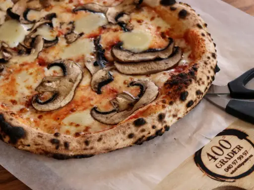 En nybakad champinjonpizza med bubblande ost, redo att skäras med saxen. En perfekt pizza för alla som gillar 400grader recensioner.