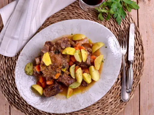 Plato de rabo de toro estofado con patatas y zanahorias, bañado en una salsa de vino blanco.