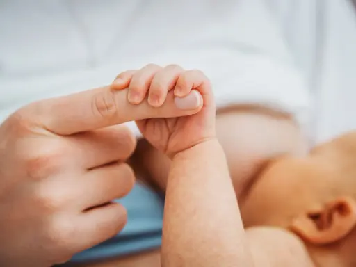 Dłoń noworodka ściska palec dorosłego. Delikatny uścisk, który budzi pytanie: czy można przekarmić noworodka?