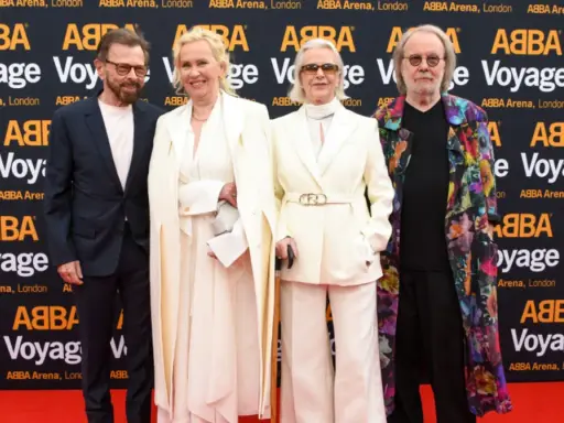 Członkowie zespołu ABBA na czerwonym dywanie, pozujący do zdjęć przed banerem "ABBA Voyage".