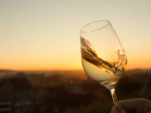 Ein Glas Scheurebe Wein schwenkt im warmen Abendlicht vor einer malerischen Landschaft.