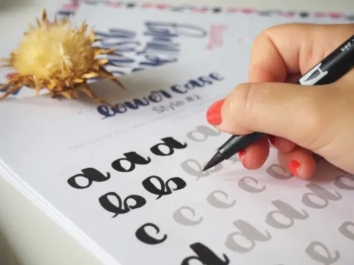 Mano practicando cómo hacer lettering con un rotulador sobre un papel con letras de ejemplo.