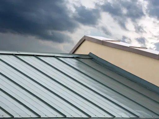 Dunkle Wolken über einem modernen Metalldach. Die glänzenden Aluminiumbahnen reflektieren das Licht, doch die Nachteile wie Geräuschentwicklung bei Regen sind nicht sichtbar.