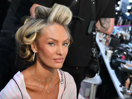 Blond włosy modelki w lokach, delikatny air touch. W tle wizażystka i kosmetyki.