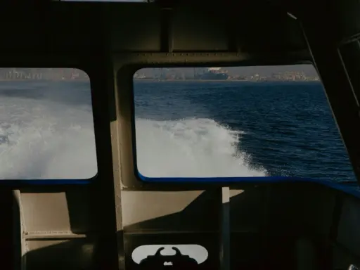 Vue depuis la cabine d'un bateau, avec le sillage blanc de l'eau. Au loin, une ville côtière et des grues de port. Les canaux VHF marine sont essentiels pour la communication.