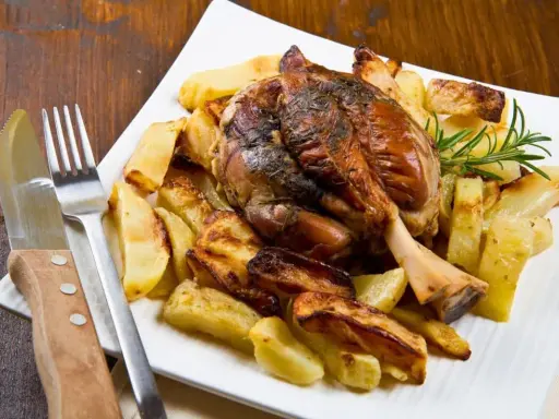 Stinco di maiale arrosto con patate croccanti, guarnito con rosmarino fresco. Un piatto succulento pronto per essere gustato.