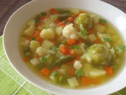 Aromaticzna jarzynowa zupa z ziemniakami, marchewką, kalafiorem i brukselką, udekorowana natką pietruszki.