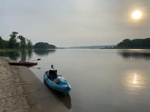 Två kajaker vid en sandstrand, redo för en paddling. Solen lyser svagt genom diset. Frågan är hur långt paddlar man på en dag?