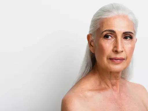 Visage femme 70 ans, cheveux argentés, regard pensif tourné vers la droite.