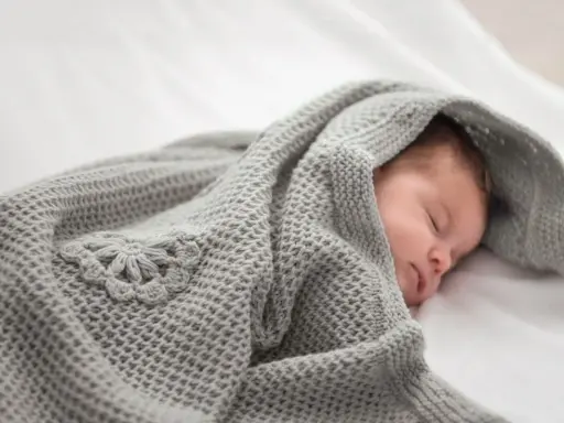 Ein schlafendes Baby, eingewickelt in eine gestrickte Babydecke mit Blumenmuster. Eine Anleitung zum Babydecke stricken wäre hier perfekt.