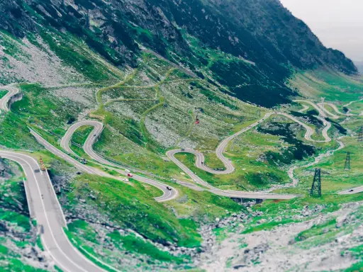 Kręta droga Transalpina wijąca się po zielonych zboczach gór. Widok z lotu ptaka na serpentyny i mosty.