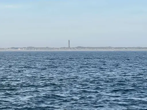 Der Leuchtturm Norderney ragt über die Dünenlandschaft am Horizont. Das weite Meer liegt davor.