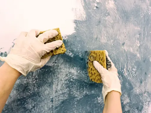 Händer med handskar målar akryl med svamp på en vägg för att skapa en texturerad effekt.