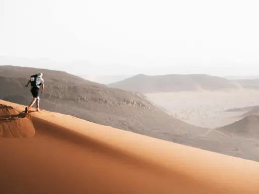Läufer erklimmt eine Sanddüne, bereit für den Marathon des Sables. Die Wüstenlandschaft erstreckt sich in der Ferne.