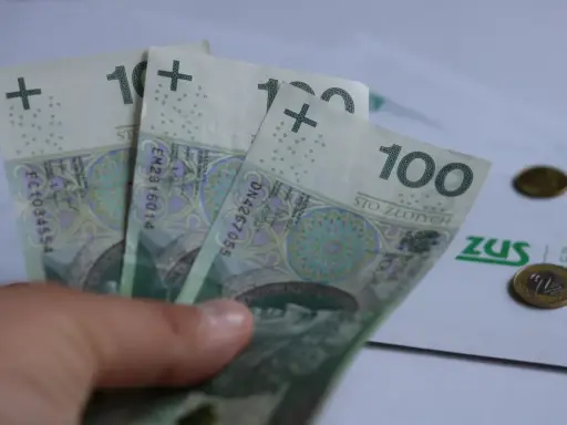 Trzy stuzłotowe banknoty w dłoni, obok dokument ZUS i monety. Czy to 30 krotność zus 2025?