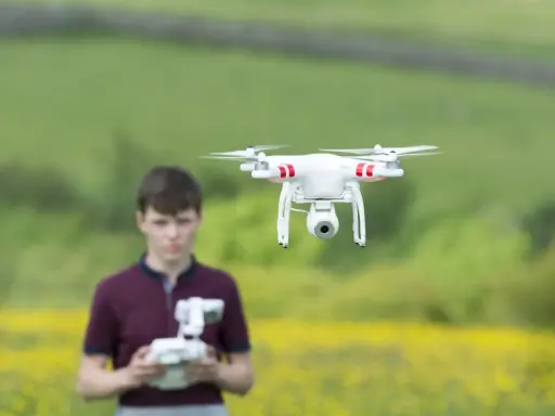 Ein Junge steuert eine Drohne in Litauen. Die Drohne schwebt über einem Feld mit gelben Blumen.