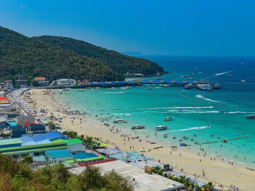 Ein belebter Pattaya Strand mit vielen Menschen, Sonnenschirmen und Booten im türkisfarbenen Meer.