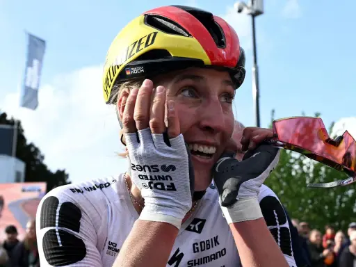 Glückliche Radfahrerin Franziska Koch mit Helm in Deutschlandfarben, die sich die Hände vors Gesicht hält.