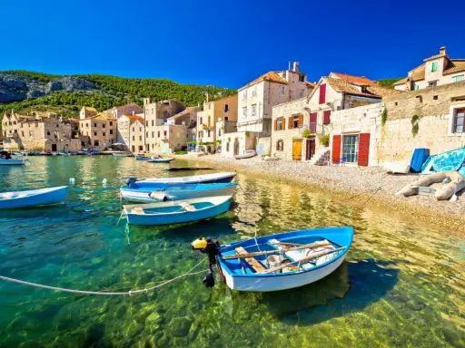 Barchette azzurre in un mare cristallino, un invito a scoprire dove andare al mare in Croazia. Case di pietra e colline verdi fanno da sfondo.