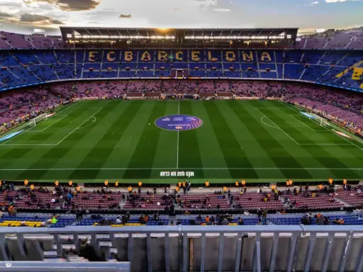 Widok na stadion Camp Nou podczas remontu, z trybunami w kolorach FC Barcelony i oświetlonym boiskiem.