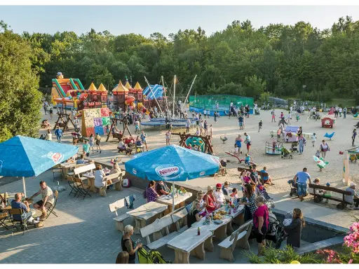 Rodzinna zabawa na placu zabaw w Ocean Park Władysławowo. Dzieci szaleją na dmuchanych zamkach, trampolinach i zjeżdżalniach, podczas gdy dorośli odpoczywają przy stolikach.