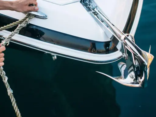 Hände halten ein Seil, das mit dem glänzenden Anker eines Bootes verbunden ist. Was ist ein Anker? Er hält das Schiff sicher am Meeresgrund.