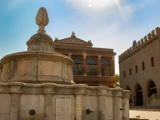 Fontana in pietra con pigna, edifici storici e cielo azzurro. Un assaggio dei monumenti di Rimini.