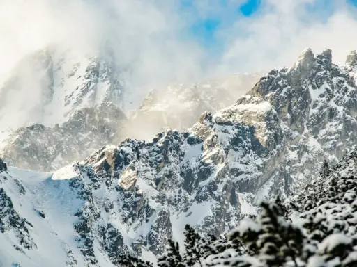 Śnieżne szczyty górskie w słońcu, z mgłą i niebieskim niebem.