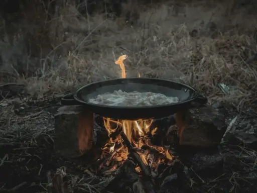 Cuisine en plein air sur un réchaud rocket stove improvisé. Une poêle cuit des aliments sur un feu vif.