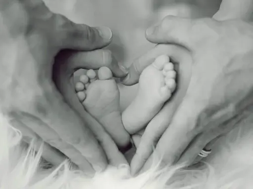 Manos de padre formando un corazón alrededor de los pies de su bebé, un símbolo de apego excesivo al padre y amor incondicional.
