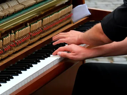 Mains sur le clavier d'un piano, prêt à jouer d'un instrument. Les marteaux et les cordes sont visibles.