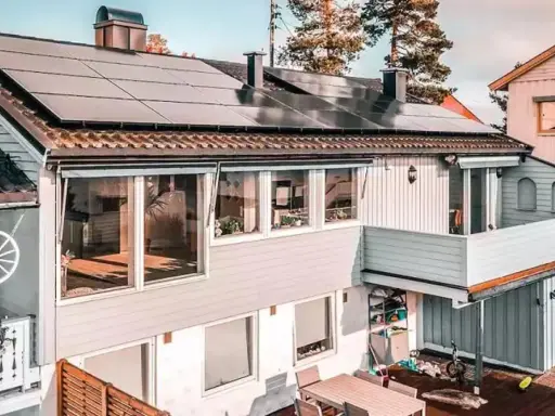 Hus med trina solceller på taket. En balkong med blommor och ett dekorativt hjul.