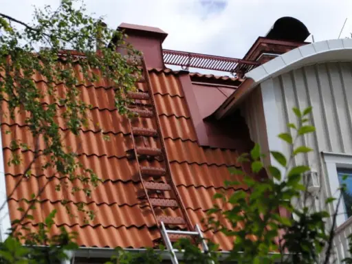 Takstege på ett rött tegeltak, en del av taket syns genom lövverk. Kanske för att följa takstege regler vid sotning.