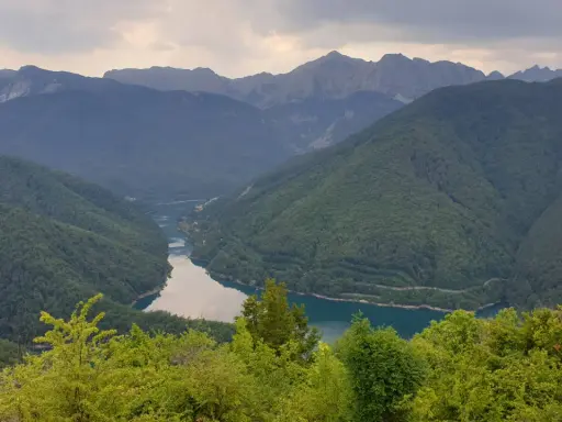 Valli boscose e un lago serpeggiante nella **Garfagnana e Lunigiana**, con montagne maestose sullo sfondo.