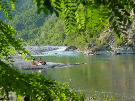 Un **lago vicino Milano con spiaggia** dove coppie si rilassano tra rocce e vegetazione lussureggiante.