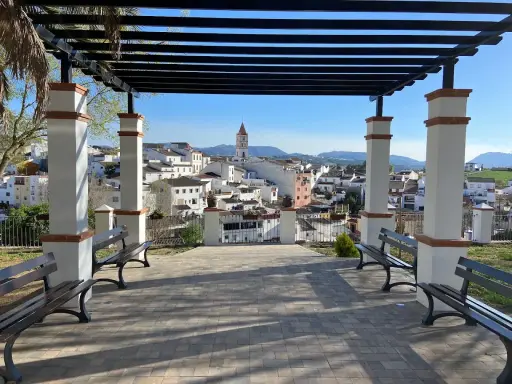 Un mirador con bancos y un arriate de flores ofrece vistas de un pueblo blanco con una torre de iglesia.