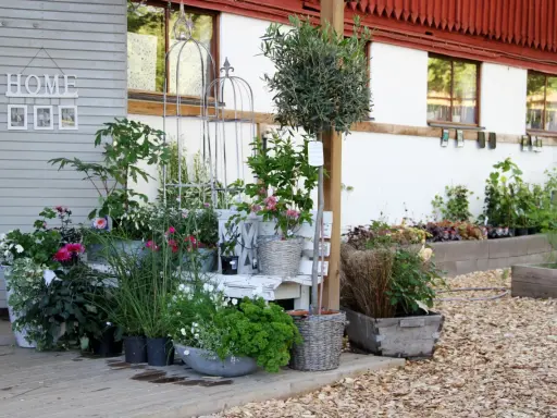 En lummig kvarnkulla trädgård med blommor i krukor och rabatter. En vit bänk och dekorativa spaljéer skapar en charmig miljö.