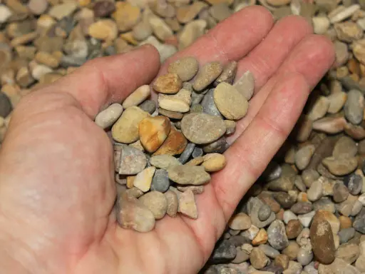 Mano sosteniendo una variedad de guijarros, mostrando que son los áridos, pequeños fragmentos de roca y minerales.