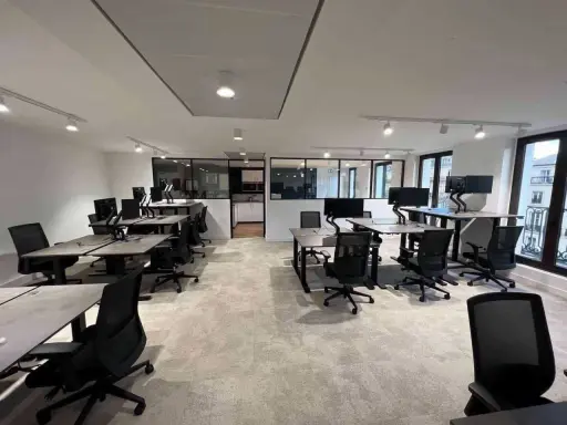 Bureau moderne avec postes de travail réglables en hauteur, écrans d'ordinateur et chaises ergonomiques. L'espace semble propre, mais on pourrait y sentir un air vicié sans fenêtres ouvertes.