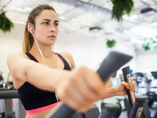Junge Frau trainiert konzentriert auf einem Crosstrainer, um abzunehmen. Sie hört Musik über Kopfhörer.