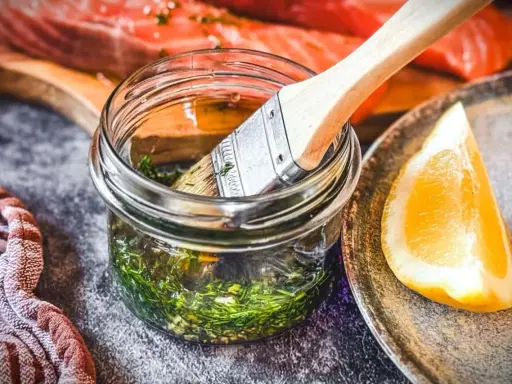 Marinade mit Kräutern und Zitrone bereit, um den Lachs zu verfeinern. Ein Pinsel liegt in der Glasflasche.