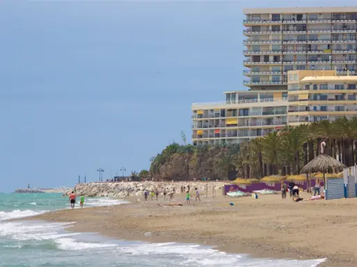 Menschen genießen den sonnigen torremolinos strand mit Palmen und einem großen Hotel im Hintergrund.