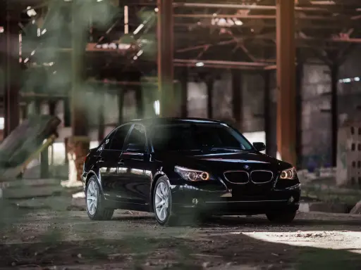Czarny BMW 535d w opuszczonej hali, otoczony mgłą i gruzem.