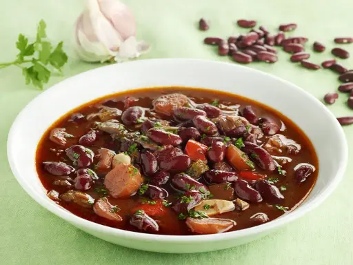 Un plato humeante de judías pintas con trozos de carne y verduras, decorado con perejil fresco.