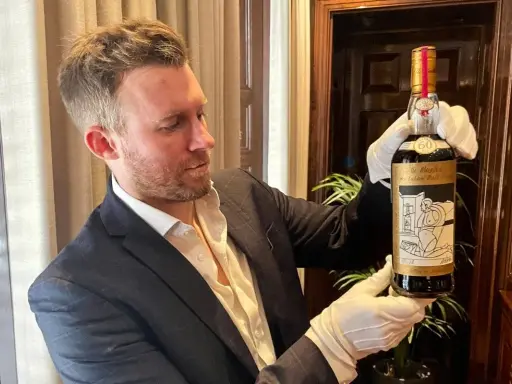 Mężczyzna w białych rękawiczkach prezentuje butelkę The Macallan 60 Year Old, jedną z najdroższych whisky świata.
