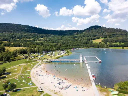 Słoneczny dzień nad zalewem w Starej Morawie. Ludzie odpoczywają na plaży i w wodzie, a w tle widać zielone wzgórza.