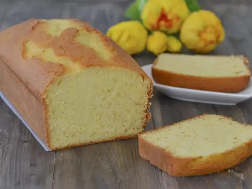 Un soffice plumcake al limone, dorato e profumato, pronto per essere gustato. Due fette sono già state tagliate, invitando a un assaggio.